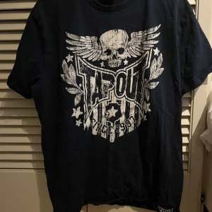 Mörk blå T-shirt med dödskalletryck från Tapout - Cool mörk blå T-shirt från Tapout med ett stort tryck av en dödskalle med vingar och texten 'Since 1997'. Perfekt för en edgy look. Kortärmad och bekväm passform.