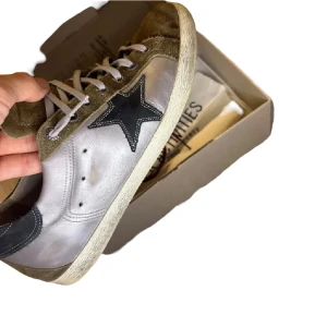 Golden Goose sneakers🫒 - Säljer ett par snygga Golden Goose sneakers i mycket bra skick. De har en cool stjärndetalj på sidan och är i en mix av grått och vitt med mocka framtill. Perfekta för både vardag och fest! Skorna kommer med originalförpackning och extra skosnören. Tar även emot byten 
