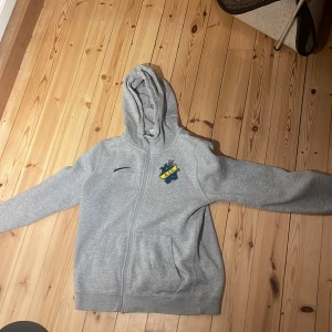Grå hoodie AIK - Säljer en grå hoodie från Nike med AIK-logga på bröstet. Tröjan har dragkedja och en bekväm huva. Storlek 147-158. Inga tecken på användning 