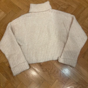 Beige stickad polotröja från Zara - Mysig beige stickad polotröja från Zara i storlek 11-12 år. Tröjan har en ribbad struktur och långa ärmar, perfekt för kyligare dagar. Den höga kragen ger extra värme och stil. Passar utmärkt till både jeans och kjol.