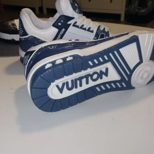 Blå och vita sneakers från Louis Vuitton - Snygga blå och vita sneakers från Louis Vuitton med tydlig logotyp på sulan och ovandelen. Skorna har snörning och ett stilrent mönster på ovandelen. Perfekta för den som vill ha en exklusiv look.