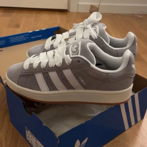 Grå Adidas Campus sneakers - Snygga grå Adidas Campus sneakers med vita detaljer och klassiska tre ränder på sidan. Skorna har en stilren design med snörning och en bekväm sula. Perfekta för en avslappnad stil. Helt nya med lapp kvar ska köpa svarta ist därav att jag säljer köptes för 1349 GÅR INTE ner i pris 