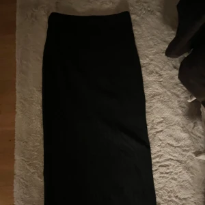 Svart ribbad långkjol - Snygg svart långkjol med ribbad struktur. Perfekt för en stilren look. Kjolen är enkel och elegant, vilket gör den lätt att matcha med olika toppar.