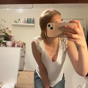 Vit ärmlös topp med spetsdetaljer - Säljer en söt vit ärmlös topp med v-ringning och spetsdetaljer på axlarna och ryggen! Perfekt för varma dagar eller som ett lager under en kofta. Toppen är i ett mjukt och bekvämt material.