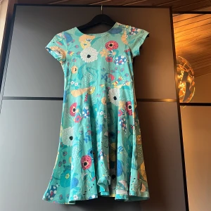 Turkos blommig klänning från Polarn O. Pyret - Säljer en söt turkos klänning från Polarn O. Pyret med ett färgglatt blommönster och fiskar. Klänningen har korta ärmar och en rund halsringning, det är en klänning gjord med otroligt mjukt material. Perfekt för sommarens äventyr! 🌸🐟Frakt betalar köparen, kan hämtas i Mölnlycke. 