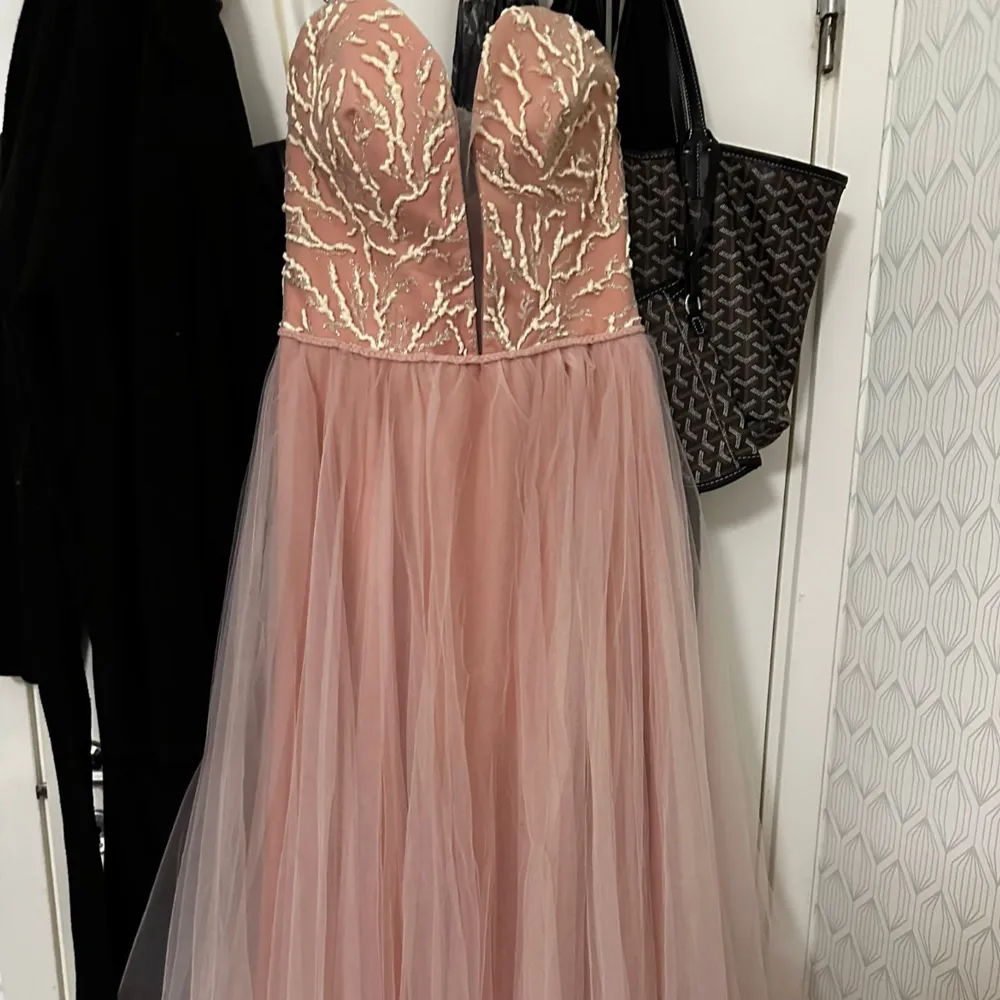 Elegant rosa långklänning med en vacker broderad överdel i guld. Klänningen har en axelbandslös design och en luftig tyllkjol som är öppen vid sidan. Perfekt nu till balen, klänningen är i väldigt bra skick då den användes bara en gång. hör av dig om du är intresserad, . Mekot.