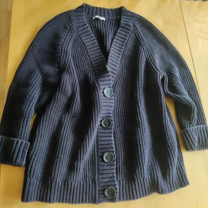 Mörkblå stickad kofta från Dagmar - Säljer en snygg mörkblå stickad kofta från Dagmar. Koftan har stora knappar framtill och ribbade detaljer vid ärmslut och nederkant. Storlek small passar även en medium. Något tvättpåverkad därav priset. 