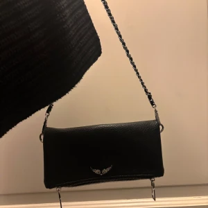 ZADIG & VOLTAIRE likande väska - rock - OBS! Kan ej garantera att den riktig, Köpt via Vinted!! Säljer denna Zaidg & Voltaire likande!! väska. Köpt på vinted i syfte för en snygg och stilren fest väska! Så kan tyvärr inte garantera att den inte är fejk samt hållbarheten!🥰 Kommer med ett långt snöre.