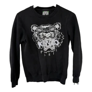 Svart sweatshirt från Kenzo - Snygg svart sweatshirt från Kenzo med ett stort tigerhuvud och texten 'Kenzo Paris' broderat på framsidan. Tröjan har långa ärmar och en rund halsringning. Perfekt för en stilren och avslappnad look.