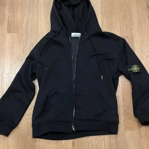 Svart hoodie från Stone Island - Säljer min svarta stone island zip up hoodie den är storlek M och är använd väldigt lite den har inga defekter och scannen fungerar. Priset är inte fast, hör av vid funderingar.