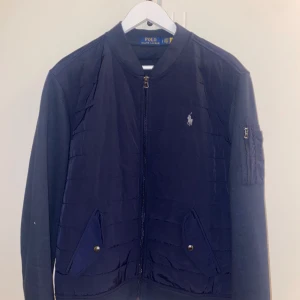 Mörkblå cardigan jacka från Polo Ralph Lauren - Snygg mörkblå cardigan jacka från Polo Ralph Lauren med dragkedja och broderad logga på bröstet. Säljer på grund av att jag aldrig använder den, den är i nyskick den är använd en gång. Har original lapp till jackan köpt förra året för 3500kr säljer nu för 1500kr prutat och klart! Perfekt jacka till dom medelvarma dagarna. Jag är 186 och väger 80kg och den passar mig bra. 