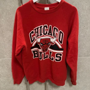 Röd Chicago Bulls sweatshirt - Säljer en röd sweatshirt med Chicago Bulls-logga på framsidan. Tröjan har långa ärmar och en klassisk rund halsringning. Perfekt för sportfantaster och streetwear-älskare. Har fått vit målarfärg på armen därav priset!