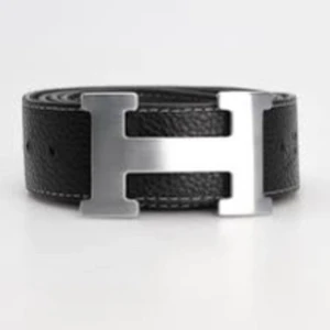 Svart bälte med silverfärgat spänne - Snyggt svart bälte i skinn med ett stort, stilrent silverfärgat H-spänne. Perfekt för att ge en elegant touch till din outfit. Bältet har en klassisk design som passar till många olika stilar.