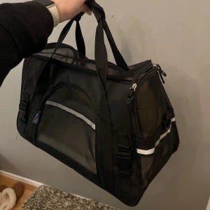 Transportbur - Säljer denna transportväska till katt eller liten hund. Den går att öppna på båda kortsidorna samt från ena långsidan. Utrustad med två förvaringsfack samt säkerhetpännen så att djuret inte kan öppna buren inifrån. Axelrem medföljer. Finns inga täcken på användning!