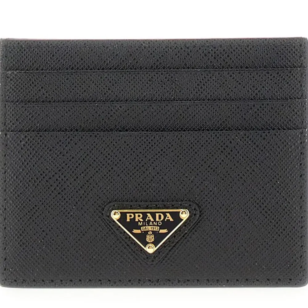Elegant svart kortfodral från Prada i skinn med plats för flera kort. Den har en stilren design med Pradas ikoniska logotyp i guld på framsidan. Perfekt för att hålla dina kort organiserade med stil. Helt ny med box ny pris 4000kr. Laukut & Käsilaukut.