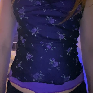 Blommig lila linnetopp - Snygg lila vintage  linnetopp med blommigt mönster. Toppen har en åtsittande passform och smala axelband. Perfekt för en somrig look!