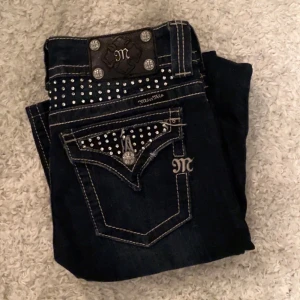 Mörkblå jeans med nitar - Snygga mörkblå jeans från Miss Me med coola nitar på bakfickorna och midjan. De har en unik design med broderade detaljer och en metallplatta med logotyp baktill. Perfekta för att ge din outfit en edgy touch. Pris kan diskuteras 