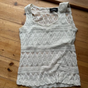 Vit spetslinne från Bon'A Parte - Säljer ett superfint vitt spetslinne från Bon'A Parte. Det har ett vackert spetsmönster och extra tyg över bysten. Perfekt för sommardagar eller att ha under en kavaj för en chic look. Linnet är i bra skick och redo för nya äventyr!