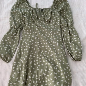 Grön blommig klänning från Shein - Säljer en superfin grön klänning från Shein med ett sött vitt blommönster. Klänningen har långa ärmar och en söt knytning vid halsen. Använd några få gånger.