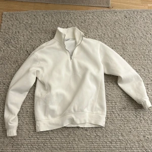 Vit tröja med dragkedja från Zara - Säljer en stilren vit tröja från Zara i storlek S. Den har en halv dragkedja vid halsen och är perfekt för en avslappnad look. Tröjan är långärmad och gjord i ett mjukt material som känns skönt mot huden. Perfekt för både vår och höst!