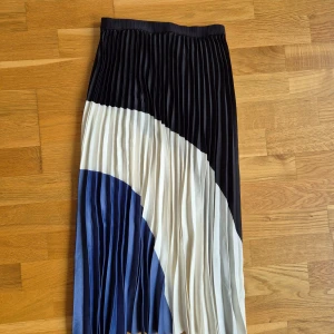 Plisserad kjol - Plisserad kjol från HM, midikjol. Nyskick, helt oanvänd. Storlek 34. Resårband vid midjan. Faller väldigt fint på kroppen. 100% polyester. Svart, vit och blå färg. 