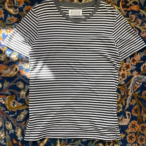 Randig t-shirt från Maison Margiela - Säljer en snygg randig t-shirt från Maison Margiela. Den är svart och vit med en grå krage. T-shirten är i bomull och har korta ärmar. Skriv om du har någon fråga. Taggad Xs men passar S