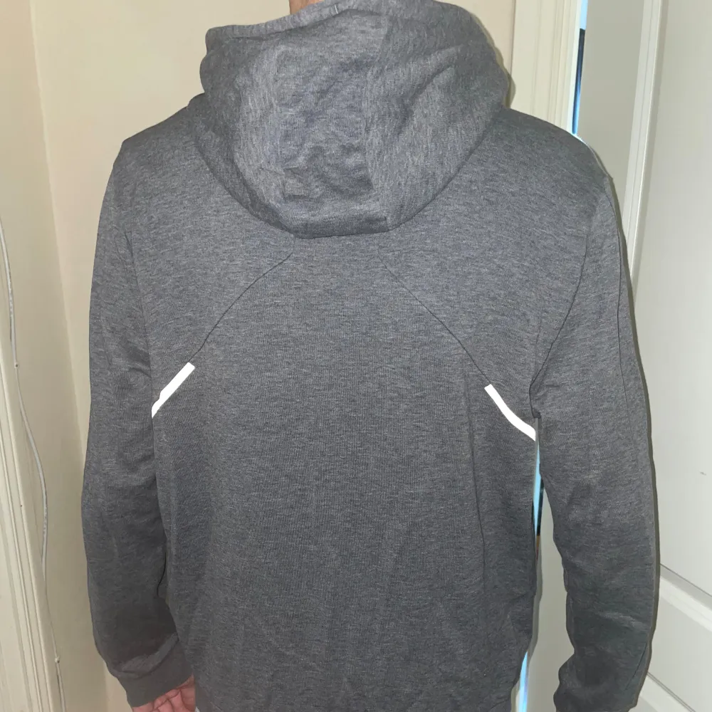 Säljer en snygg grå hoodie från BOSS med dragkedja och huva. Den har vita detaljer och en logga på bröstet. Perfekt för en casual look eller när du vill hålla det stilrent. Passar både till vardags och chillkvällar.. Tröjor & Koftor.