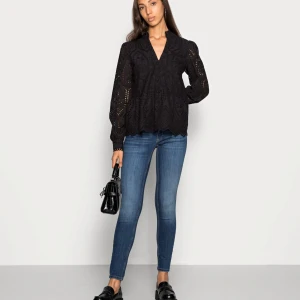 Svart blus med spetsdetaljer - Snygg svart blus med v-ringning och spetsdetaljer. Den har långa ärmar och ett fint mönster som ger en elegant touch. Perfekt för både vardag och fest!