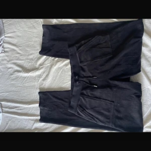 Svarta mjukisbyxor från Juicy Couture - Säljer ett par svarta mjukisbyxor från Juicy Couture i storlek L. De är superbekväma med en elastisk midja och snörning. Perfekta för en avslappnad dag hemma eller en snabb tur till affären. Byxorna har praktiska fickor och är i mycket bra skick.