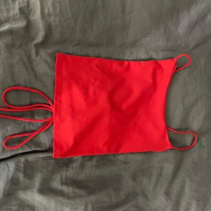 Röd korsettopp med snörning - Snygg röd korsettopp med smala axelband och snörning i ryggen. Perfekt för en utekväll eller fest! Toppen är i ett mjukt och stretchigt material som sitter bekvämt på kroppen.