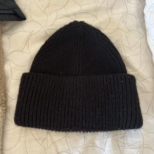 Svart mössa - Säljer en svart stickad mössa i nyskick. Perfekt för kalla dagar med sin ribbade design som ger extra värme och stil. Passar både till vardags och mer avslappnade tillfällen. Enkelt att matcha med olika outfits!