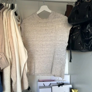 Grå stickad topp från Lindex - Säljer en superfin beige stickad topp från Lindex. Den har en mysig och avslappnad stil med korta ärmar och ribbade detaljer vid hals och nederkant. Perfekt för lager-på-lager under hösten eller våren. Passar både till vardags och lite mer uppklädda tillfällen. 🧶✨