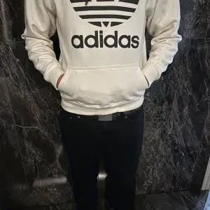 Säljer en snygg vit hoodie från Adidas med deras klassiska logga i svart på framsidan. Den har en stor ficka framtill och en bekväm huva. Perfekt för en avslappnad stil eller träning. Passar till allt och är superbekväm! 🖤