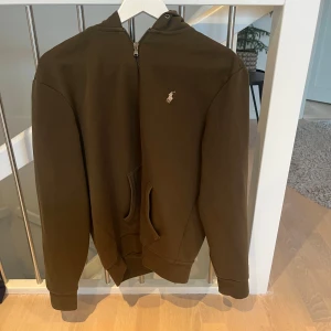 Grön hoodie från Polo Ralph Lauren - Säljer en snygg grön hoodie från Polo Ralph Lauren i storlek M. Den har en dragkedja framtill och en liten logga på bröstet. Perfekt för höst och vår, och den är superbekväm att ha på sig. Passar både till vardags och lite mer avslappnade tillfällen. 🧥