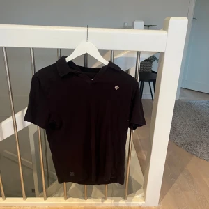 Marinblå kortärmad pikétröja - Säljer en stilren marinblå pikétröja i bomull. Den har en klassisk krage och en liten broderad detalj på bröstet. Perfekt för både vardag och festliga tillfällen. Passar bra till jeans eller chinos!