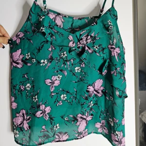 Turkos blommig linnetopp - Superfin turkos linnetopp med rosa blommor storlek 40/42 eller L. Toppen har smala axelband och söta volanger framtill. Materialet känns lätt och luftigt, liknar mesh. Oanvänt utan defekter. 