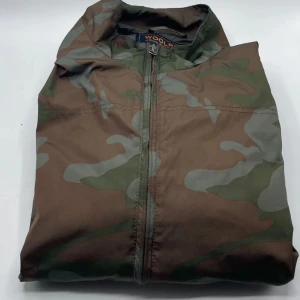 Woolrich windbreaker  - Tja! Säljer en fet grön camouflage windbreaker från Woolrich! En riktigt skön vår och höst jacka men funkar även i varm vinter till ett riktigt bra pris!🫣 Använt den i ca 1,5 månad!✌️snabb affär=lägre pris!🙏🤙