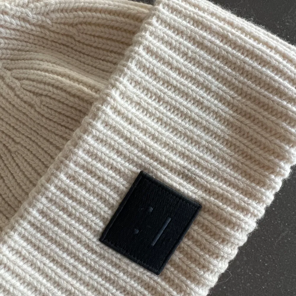 Säljer en superfin beige stickad mössa från Acne Studios. Den är ribbad och har en svart patch framtill som ger en cool touch. Perfekt för att hålla sig varm under höst och vinter. Mössan är i bra. skick och passar de flesta tack vare sin stretchiga design. Har lite sminkfläckar på insidan! . Accessoarer.