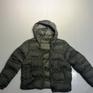 Grön pufferjacka från Zara - Säljer en grön pufferjacka från Zara. Jackan har en dragkedja framtill och är långärmad med en mysig huva. Perfekt för kyliga dagar. Nypris 1000kr