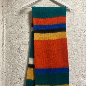 Flerfärgad randig halsduk - Säljer en färgglad och mysig halsduk med breda ränder i orange, blå, grön, gul, svart och vit. Perfekt för att liva upp vinter- och höstgarderoben. Halsduken är stickad och ger en varm och skön känsla.