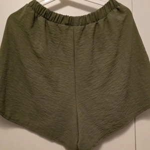 Olivgröna shorts med resårmidja - Snygga olivgröna shorts med en bekväm resårmidja. Perfekta för en avslappnad stil, dessa shorts har en lös passform och är tillverkade i ett lätt material som ger en skön känsla. Perfekta för varma dagar!