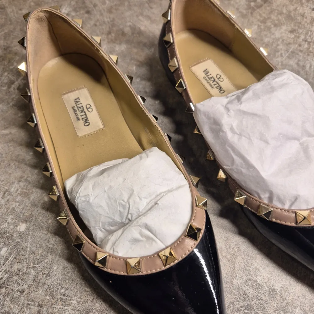 Snygga svarta ballerinaskor från Valentino med spetsig tå och ikoniska nitar runt kanten. Skorna har en elegant design som passar perfekt för en stilren look.. Kengät.