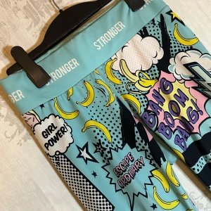 Tights & topp från Stronger ❤️ - Snygga och unika leggings från Stronger med ett färgglatt serietidningstryck. De har text som 'Girl Power' och 'Escape Ordinary' i popkonststil. Perfekta för att sticka ut med sitt lekfulla mönster och starka färger. Matchande topp! Allt i storlek S