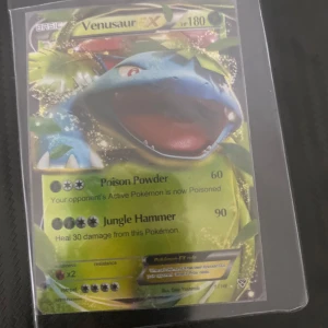 Venusaur EX Pokémonkort - Säljer ett Venusaur EX Pokémonkort med 180 HP. Kortet har attacker som Poison Powder och Jungle Hammer. Perfekt för samlare eller spelare som vill förstärka sin kortlek.