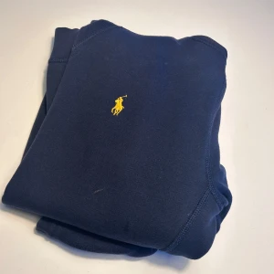 Mörkblå hoodie från Ralph Lauren - Säljer en snygg mörkblå hoodie från Ralph Lauren med det klassiska gula logotypen på bröstet. Perfekt för en avslappnad stil med sin mjuka och bekväma passform. Den har långa ärmar och en praktisk huva. Väldigt bra skick! 