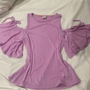 Lila topp med öppna axlar - Säljer en lila topp från Gina med öppna axlar och knytband. Toppen har korta ärmar med volangdetaljer och är tillverkad i ett mjukt material.