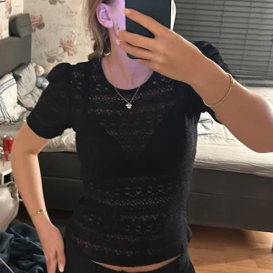 Svart spetsblus från Vila - Elegant svart spetsblus från Vila med korta puffärmar och rund halsringning. Blusen har ett vackert spetsmönster och en knappdetalj i nacken. Perfekt för en stilren look.