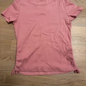 Rosa ribbad topp  - Säljer en söt rosa ribbad topp. Den har en knytning på sidorna som ger en fin detalj. Perfekt för en avslappnad stil. Storlek 156-164