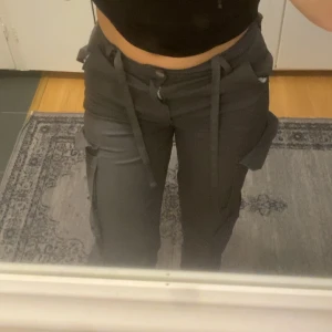 Gråa cargo - Snygga gråa cargopants med snörning i midjan och flera praktiska fickor. Perfekta för en avslappnad och trendig stil. Byxorna har en loose passform och är tillverkade i ett slitstarkt material.