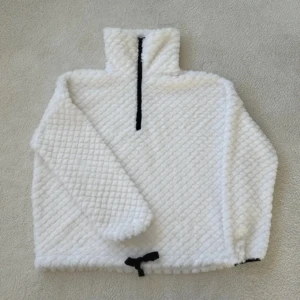 Vit fleece tröja från Women'secret - Mysig vit fleece tröja från Women'secret med halv dragkedja och hög krage. Perfekt för kyliga dagar med sin fluffiga textur och justerbar nederkant. En stilren och bekväm tröja för alla tillfällen.